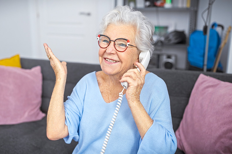 older-woman-talking-landline-telephone An older smiling woman is talking on her corded phone.