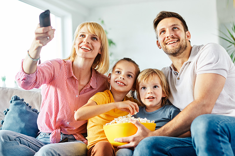 parents-children-watching-tv-together A family is watching TV and eating popcorn.