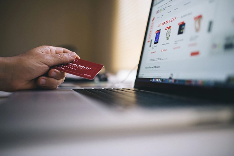 A person with credit card in hand in front of a computer monitor as they shop online.