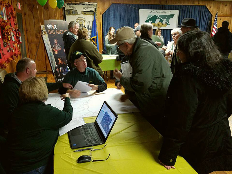 A group of people are standing in front of a table at an MTC event.