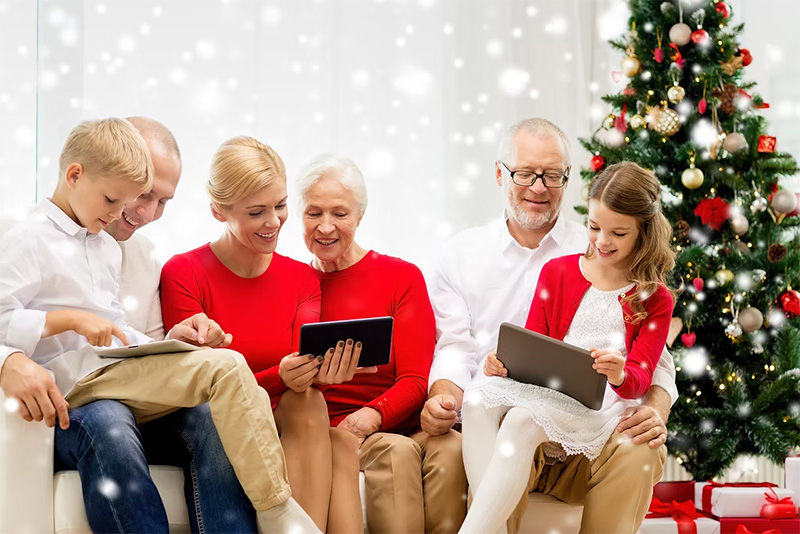 A family sitting together in front of a Christmas tree holding tablets.