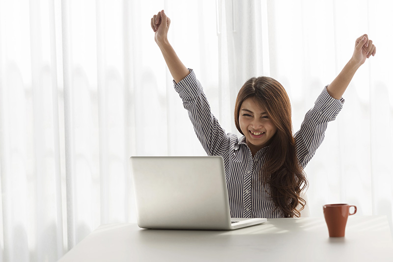 A woman in a cheering position in front of her laptop computer.