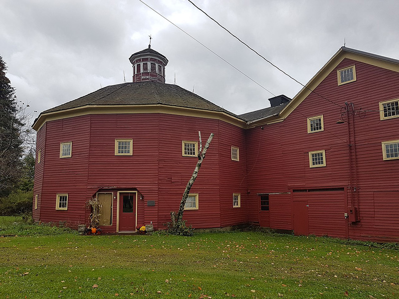 Large red barn-style building with multiple sections and small windows on a grassy lot.